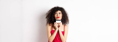 Romantik görünen genç bir kadın, elinde plastik kredi kartıyla alışverişi düşünüyor, beyaz arka planda dikiliyor. Boşluğu kopyala