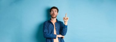 Yakışıklı bir adamın bir fikir sunduğu, parmağını kaldırdığı ve mavi arka planda durup düşünerek kafasını kaldırdığı bir görüntü. Boşluğu kopyala