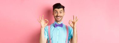 Gülümseyen, gülümseyen yakışıklı bir adam. Onaylanmış güzel jestler yapıyor. İyi seçimi övüyor, reklamları seviyor, pembe arka planda duruyor..