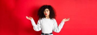 Kim bilir? Kıvırcık saçlı, omuz silkmiş, kafası karışmış, kırmızı arka planda sıradan kıyafetlerle duran cahil bir genç kadın..