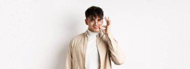 Gülümseyen kurnaz adam fermuarla ağzını kapattı, dudaklarına yakın fok hareketini gösterdi, sinsi gülümsedi, bir sır sakladı, beyaz arka planda durdu..