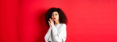 Kıvırcık saçlı, kırmızı dudaklı, yüzü makyajlı, kırmızı arka planda duran şehvetli ve romantik kız..