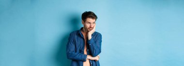 Yorgun ve sıkkın bir adam, boş kafasıyla başka bir yere bakıyor, bir kenara bakıyor, mavi arka planda duruyor..