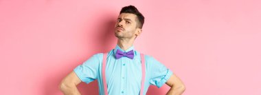 Bıyıklı, papyonlu, gururlu, kendine güvenen beyaz adam. Çenesi yukarıda, kaşlarını çatmış, pembe arka planda duran kameraya bakıyor..