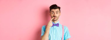 Meraklı mutlu adam dudağa dokunuyor, kameraya dalgın dalgın bakıyor, ne alacağına karar veriyor, pembe arka planda duruyor..