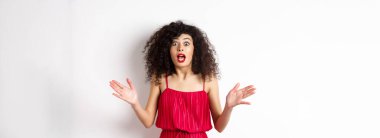 Kıvırcık saçlı heyecanlı bir kadın, şaşkın yüzüyle konuşuyor, büyük haberleri açıklıyor, el sıkışıyor ve beyaz arka planda kameraya hayret içinde bakıyor..