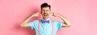 Rahatsız genç adam blok gürültü, kulaklar kapalı eller ve çığlıklar rahatsız edici yüksek ses, pembe arka plan üzerinde durmak.