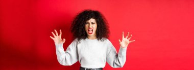 Korkutucu kadın seni korkutmaya çalışıyor, bağırıyor ve hayvan pençeleri gösteriyor, insana bağırıyor, kırmızı arka planda duruyor..