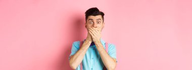 Şok olmuş ve nutku tutulmuş adam ağzını kapattı, elleriyle dudaklarını kapadı ve kameraya baktı, pembe arka planda duruyordu..