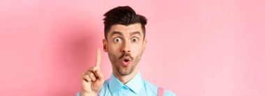 Heyecanlı bir adamın fikir ileri sürdüğü, parmağını kaldırdığı ve öneri dediği yakın plan, pembe arka plan üzerinde durmak. Boşluğu kopyala