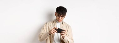 Cep telefonuyla video oyunu oynayan yakışıklı bir gencin portresi, akıllı telefonu yarış için eğmek, beyaz arka planda durmak..