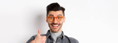 Gözlüklü, mutlu, destekleyici gülümseyen, övgü dolu, beyaz arka planda duran, havalı bir mağaza öneren, heyecanlı ve komik bir adamın portresi..