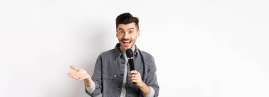 Mikrofonla konuşan, el kol hareketi yapan, mikrofonla konuşma yapan, beyaz arka planda duran yakışıklı bir sanatçı..