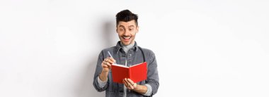 Ajandasında yazan, gülümseyen, günlük ya da günlüğe fikirler yazan, beyaz arka planda duran heyecanlı adam..