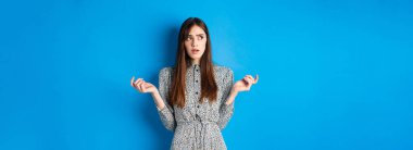 Kafası karışmış tatlı kız bir şeyi anlayamaz, dalgın dalgın bakar ve parmaklarını sayar, mavi arka plan karşısında elbise giyer..