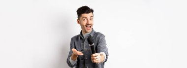 Yakışıklı gülümseyen adam mikrofonla elini uzatıyor, mikrofonu sana veriyor, beyaz arka planda duruyor..