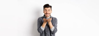 Tatlı genç adam kameraya hava öpücüğü yolluyor ve gülümsüyor. Umutsuz romantik aşkını gösteriyor, elinde bir şey tutuyor, beyaz arka planda duruyor..