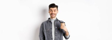 Hevesli yakışıklı bir adam kahve fincanı tutuyor ve gülümsüyor, kafeteryadan güzel bir içki içiyor, beyaz arka planda duruyor..