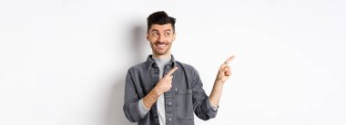 Mutlu yakışıklı adam gülümsüyor ve solu işaret ediyor, havalı ürünler gösteriyor, beyaz arka planda duruyor..