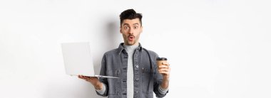 Heyecanlı adam der ki: Vay canına, iş için dizüstü bilgisayarı, kağıt bardakta kahveyi, beyaz arka planda duran.