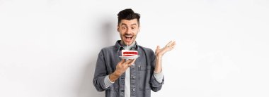 Doğum gününü kutlayan heyecanlı adam, mumla doğum günü pastasına mutlu bakıyor, dilek diliyor, beyaz arka planda mutlu duruyor..