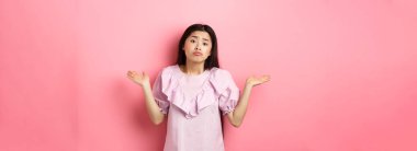 Üzgünüm yardımcı olamam. Hüzünlü suratlı, hiçbir şey bilmeyen, pembe arka planda kararsız duran cahil Asyalı kız..