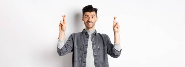 Umut gerçek olur. Pozitif ve yakışıklı adam umut dolu görünüyor ve kameraya gülümsüyor, sonuçları bekliyor, beyaz arka planda duruyor..