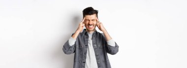 Baş ağrısı çeken, baş ağrısından dişlerini sıkan, baş şakaklarına dokunan, migren ağrısı çeken, beyaz arka planda duran, ağrı kesicilere ihtiyacı olan bir adam..