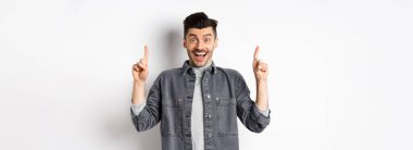 Heyecanlı yakışıklı adam parmak kaldırıyor, gülümsüyor, mutlu ve özel bir anlaşma yapıyor, beyaz arka planda duruyor..