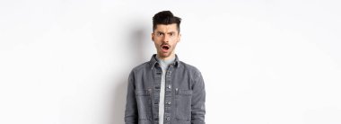 Şok olmuş ve gücenmiş bir adam, kameraya açık ağızla bakıyor, acımasız sözlerle incinmiş, beyaz arka planda hayal kırıklığına uğramış..