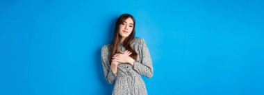 Romantik, güzel bir kadın, elini kalbe koyuyor, nazikçe gülümsüyor, tatlı anılarını saklıyor, mavi arka planda duruyor..