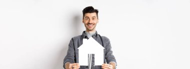 Gayrimenkul ve sigorta konsepti. Yakışıklı genç adam gazete kupürlerini gösteriyor ve gülümsüyor, daire arıyor, mülk satın alıyor, beyaz arka plana karşı duruyor..