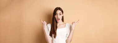 Şaşırmış genç bir kız solu ve sağı işaret ediyor, nefes nefese ve hayret verici diyor, iki havalı seçenek gösteriyor, bej arka plan.