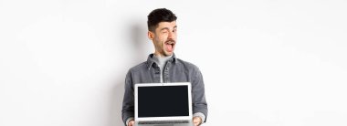 Neşeli adam göz kırpıyor ve boş akıllı telefon ekranı gösteriyor, size reklam sunuyor, beyaz arka planda duruyor..