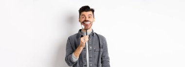 Yakışıklı, pozitif adam beyaz arka planda duran büyüteçle beyaz, kusursuz gülümseme sergiliyor..