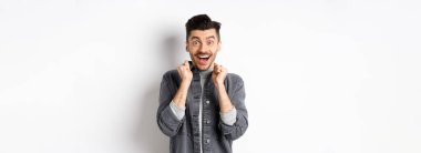 Heyecanlı genç adam mutluluktan atlıyor, şaşırmış bir şekilde gülümsüyor ve el ele tutuşuyor, beyaz arka planda duruyor..