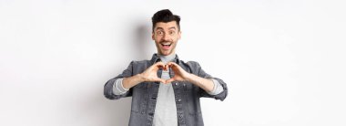 Romantik erkek arkadaş kalp hareketi yapıyor ve kameraya aşkla bakıyor, Sevgililer Günü 'nden sonraki beyaz arka planda dikilerek Beyaz' ı kutluyor. Romantizm kavramı.