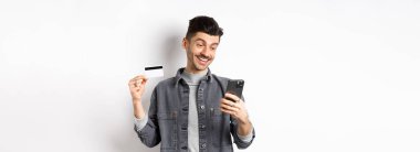 İnternetten alışveriş konsepti. İnternetten alışveriş yapan yakışıklı bir adam. Plastik kredi kartı gösteriyor. Akıllı telefona bakıyor..