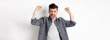 Motive olmuş genç adam bağırıyor ve ellerini kaldırıyor, maç seyrediyor ve takımı destekliyor, tezahürat yapıyor ve tezahürat yapıyor, beyaz arka planda duruyor..