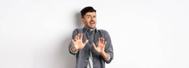 - Benden uzak dur! Korkmuş genç bir adam çığlık atıyor ve durmak istiyor, geri çekiliyor ve korkmuş görünüyor, kötü bir şeyi reddediyor, beyaz arka planda duruyor..