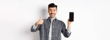 Neşeli stil sahibi adam boş akıllı telefon ekranı ve afişler gösteriyor, online alışveriş ve e-ticaret kavramı.