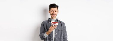 Doğum günü pastasında dilek tutan mutlu çocuk, gülümseyen ve yanan muma bakan heyecanlı, beyaz arka planda duran.