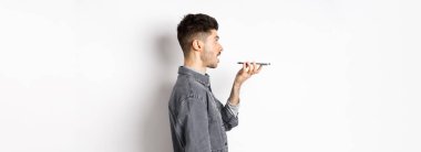 Akıllı telefonda konuşan genç adamın profili, sesli çeviri uygulaması ile tercüme edin, cep telefonu hoparlörüne konuşun, beyaz arka planda durun..