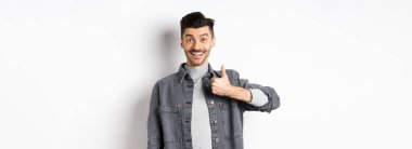 Heyecanlı yakışıklı adam baş parmağını gösteriyor ve gülümsüyor, iyi bir şey gibi, harika seçimi övüyor, tatmin olmuş ve mutlu görünüyor, beyaz arka planda duruyor..
