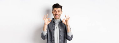 Mutlu adam evet diyor, gülümsüyor ve iyi işaretler gösteriyor, iyi ürün gibi, onaylamak için başını salla ve tatmin ol, mükemmel bir iş çıkarıyorsun, beyaz arka planda duruyorsun..