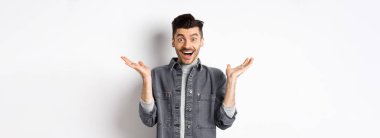 Heyecanlı genç adam sevinçten havalara uçuyor, ellerini yana açıyor ve mutlu görünüyor, şaşkın şaşkın gülüyor, beyaz arka planda duruyor..