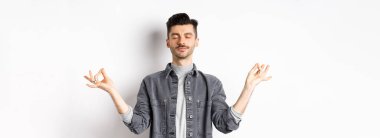 Sakin adam huzurlu bir yüzle meditasyon yapıyor, Zen Mudra tabelasında el ele tutuşuyor ve gözlerini kapatıyor, yoga yapıyor, beyaz arka planda dinleniyor..