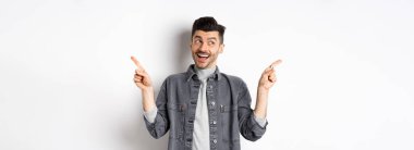 Mutlu stil sahibi adam gülüyor, yan yan işaret ediyor, iki seçenek gösteriyor, tanıtım teklifleri sunuyor ve gülümsüyor, beyaz arka plana karşı duruyor..