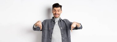 Bıyıklı, mutlu, beyaz bir adam. Gülümsüyor ve özel bir anlaşma yapıyor. Buraya bakmaya davet ediyor, beyaz arka planda duruyor..