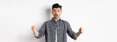 Kafası karışmış bir adam büyük bir nesne tutuyor ve şok olmuş görünüyor, büyük bir şeyi şekillendiriyor, beyaz arka planda duruyor..